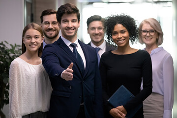 Happy diverse employees with young male leader or boss in front meet welcome new worker into team. Smiling businessman stretch hand for handshake with newcomer in office. Recruitment concept.