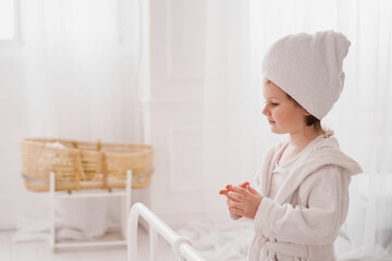 Smiling little girl in a white bathrobe after a bath. White cozy interior.