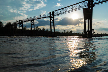 Fototapeta premium Beautiful waves of the river, on the far background, the old iron structure and a beautiful sunset.