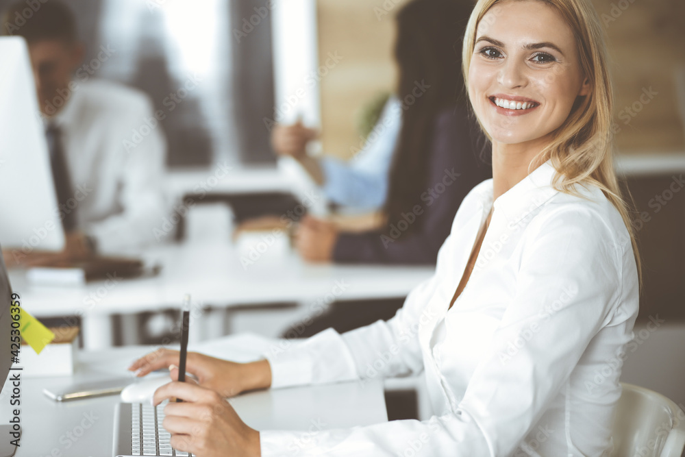 Wall mural Business woman using computer at workplace in modern office. Secretary or female lawyer smiling and looks happy. Working for pleasure and success