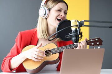 Fototapeta na wymiar Woman sings and plays guitar with headphones in front of microphone