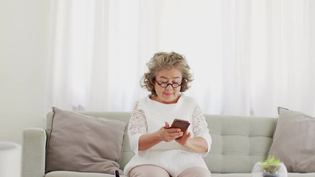 Happiness elderly asian woman with white hairs sitting on sofa using mobile phone and social media smile at home,Senior lifestyle at home concept