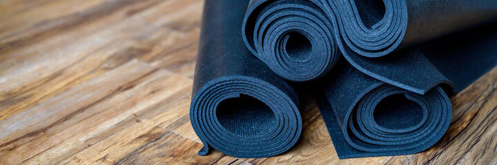 several rolled yoga or fitness rubber mats black color on wooden floor. sport accessories. banner