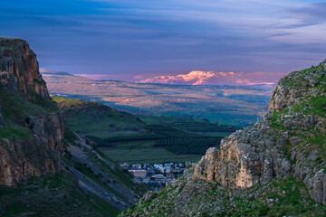 Fototapeta na wymiar Beautiful view of Galilee from the cliff of Mount Arbel National Park and Nature Reserve, with the snow-capped Mt Hermon lit up by pink sunset light in the distance; Lower Galilee, Israel
