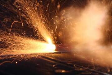 Exploding firecracker spraying sparks and causing smoke  in the dark on a dark background.