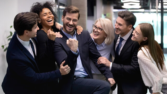 Overjoyed young male employee feel euphoric with business success or achievement, diverse colleagues congratulate. Happy multiethnic businesspeople have fun greeting coworker with victory.