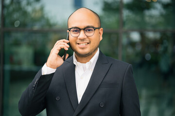 Young indian businessman using smartphone standing in front of building office. Asian businessman using in suit using on cellphone.