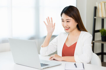 Young asian beautiful business woman working with laptop sitting at home. Smiling charming happy young female doing homework meeting conference with team at home.
