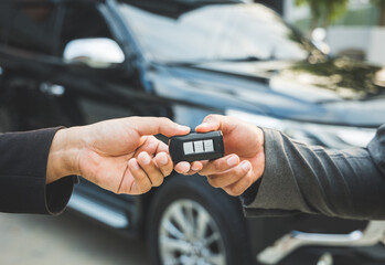 Close up businessman in suit his hands showing or giving car key for customer getting new car. Buy sell rent car concept.