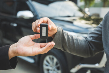 Close up businessman in suit his hands showing or giving car key for customer getting new car. Buy sell rent car concept.