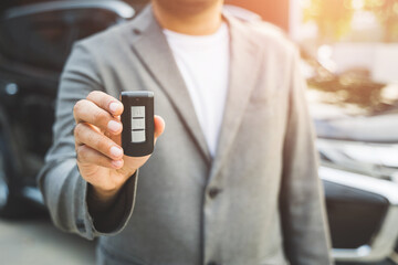 Close up businessman in suit his hands showing or giving car key for customer getting new car. Buy sell rent car concept.
