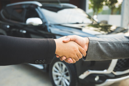Two businessmen made a deal to buy a used car, he made a contract and stood shaking hands in front of the car.