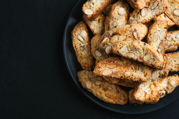 Cantuccini biscotti with almonds on a black plate on a dark background top view copy space close-up.
