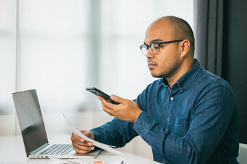 A young man is using a smartphone to scan the bill to calculate his income and expenses. In his...
