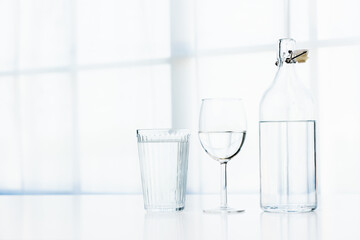 A glass of water and a clear glass water bottle are placed on the table in the house on a white background.