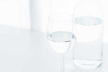 A glass of water and a clear glass water bottle are placed on the table in the house on a white background.