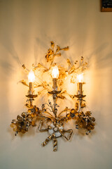 Gold three-lamp floor lamps, decorated with floral patterns on the wall. Interior details of an old villa in Italy.