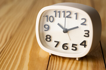 Small white alarm clock, black numbers, set the time for 10.10 o'clock, placed on a wood table.