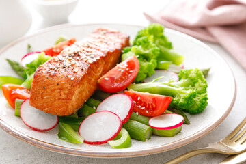 Salmon fish fillet grilled and vegetable salad with radish, tomato, green pepper, broccoli and asparagus.