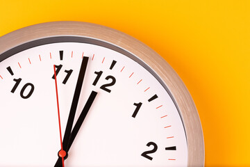 Large white alarm clock, black numbers, set the time placed on a table. Clock on isolated yellow background.