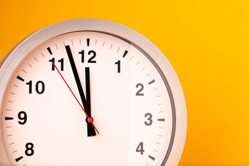 Large white alarm clock, black numbers, set the time placed on a table. Clock on isolated yellow background.