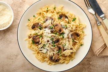 Dining italian pasta risoni, mushrooms, sauce, Parmesan, thyme, garlic, olive oil, in white plate over slate, stone or concrete background. Top view with copy space. Italian cuisine.