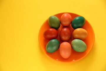 Obraz premium Colorful easter eggs on orange plate clsoe up, yellow background, copy space