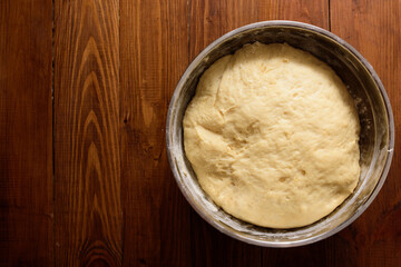 Raw yeast dough resting and rising in large metal bowl on dark wooden background.