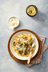 Dining italian pasta risoni, mushrooms, sauce, Parmesan, thyme, garlic, olive oil, in white plate over slate, stone or concrete background. Top view with copy space. Italian cuisine.