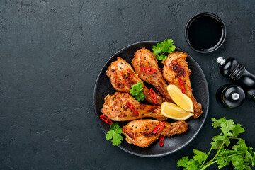 Grilled chicken drumsticks or legs or roasted bbq with spices and tomato salsa sauce on a black plate. Top view with copy space.