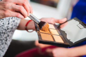 Close up of a beutician's hand holding brush while applying face powder from color pallete.