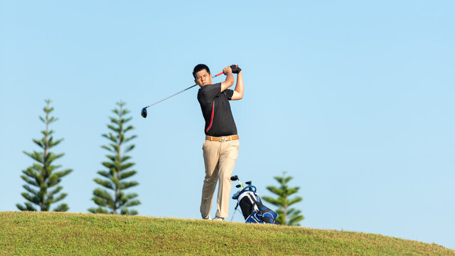Golfer asia man approach on tee off for swing and hitting golf ball on slope green and looking fairway in course. Hobby playing game golf in holiday 