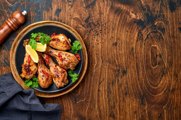 Grilled chicken drumsticks or legs or roasted bbq with spices and tomato salsa sauce on a black plate on old wooden background. Top view with copy space.