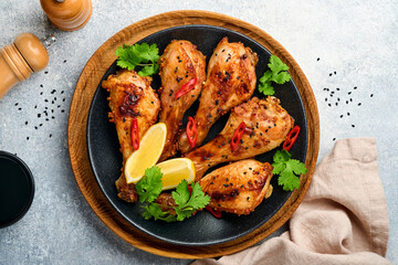 Grilled chicken drumsticks or legs or roasted bbq with spices and tomato salsa sauce on a black plate on light grey slate, stone or concrete background. Top view with copy space.