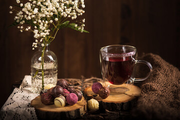 Teezeit in rustikal Still. Schleier Kraut liegt als Deko auf dem Holztisch. Glas  Tee steht auf dem Holzhintergrund, bunte Pralinen liegen liegen auf dem Stück Holz