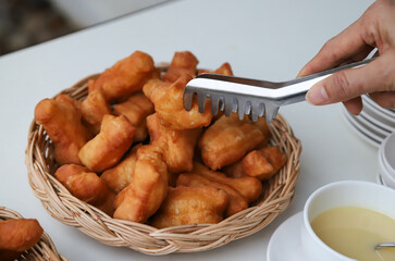 Closeup of fresh golden brown deep fried crispy oriental doughnuts in bamboo basket with woman's hand and clamp.
