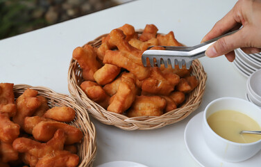 Closeup of fresh golden brown deep fried crispy oriental doughnuts in bamboo basket with woman's hand and clamp.