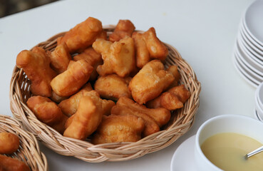 Closeup of fresh golden brown deep fried crispy oriental doughnuts in bamboo basket on white table. 
