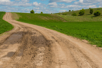 Dirt road among green fields and hills on a sunny day.