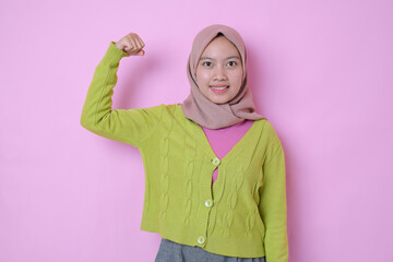 Strong powerful young muslim Asian girl wears muslim casual t-shirt with headscarf, raises arm,...