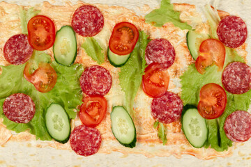 sliced fresh vegetables lie on thin pita bread with ketchup and mayonnaise sauce. salami sausage, cucumber and lettuce. close-up