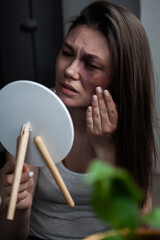 Domestic violence, abuse woman with bruise on face by the window looks in the mirror