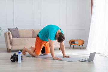 Online workout at home - middle-aged man during home yoga workout. He stretches his back in front...