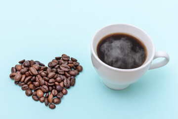 Steaming coffee cup, heart shaped coffee beans on a blue background, copy space. Morning coffee for loved ones