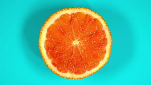 Blood orange slice rotating top view on light blue background.Macro food.Looped rotation.Healthy eating concept.Organic fresh harvest.healthy food,bio food.red fruit.