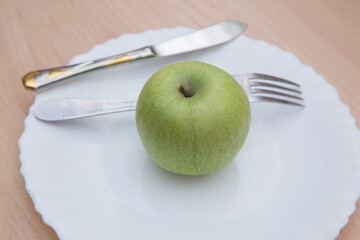 A green apple on a white plate. The concept of proper nutrition.