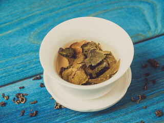 green tea is brewed in a white bowl on a blue wooden background. Dry tea leaves lie nearby. Top view