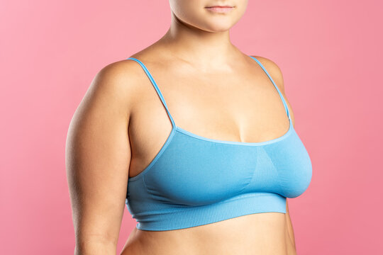 Big natural breasts in blue bra close-up on pink background