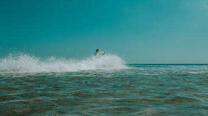 A man on a jet ski ride, the sea and the ocean in clothes, hot weather with the rays of the bright sun and white clouds against the background of the blue sky and blue transparent water with splashes