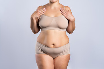 Fat woman in beige underwear on gray background, overweight female body